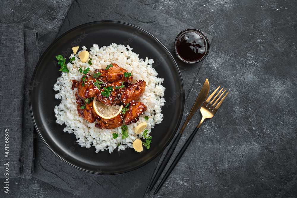A portion of rice with chicken teriyaki with sesame and parsley on a black background. A portion of rice with chicken teriyaki with sesame and parsley on a black background.