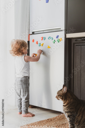 little cute toddler playing with toy letters on the fridge