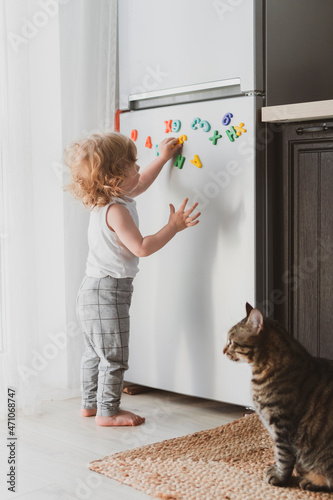 little cute toddler playing with toy letters on the fridge