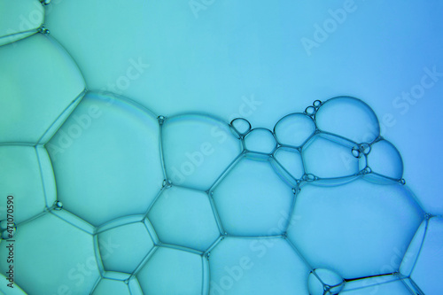 The surface of the bubbles. Extreme close-up of soap foam structure on green and blue. Cosmetic background with copy space