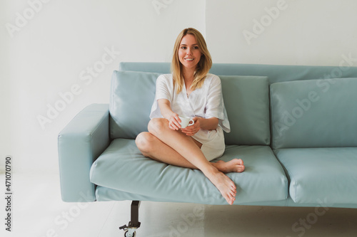 Free Download portrait of a young charming woman in a silk robe with cup of coffee at home on the sofa - GFXLoad