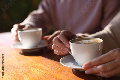 Couple with cups of aromatic coffee at wooden table in cafe, closeup