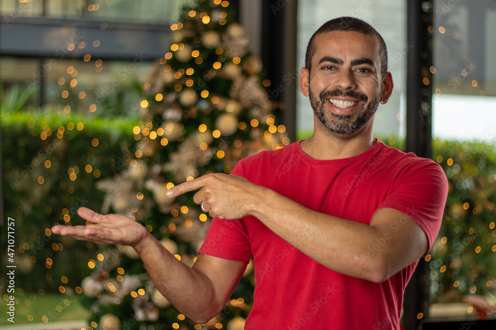 brunette man smiling, wearing red blouse showing his hand to the side, in  the background beautiful christmas decoration Stock Photo | Adobe Stock
