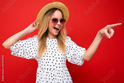 Portrait of beautiful fascinating emotional positive joyful happpy female promoter pointing to the side at copy space for advertising wearing hipster outfit isolated over background wall with empty photo