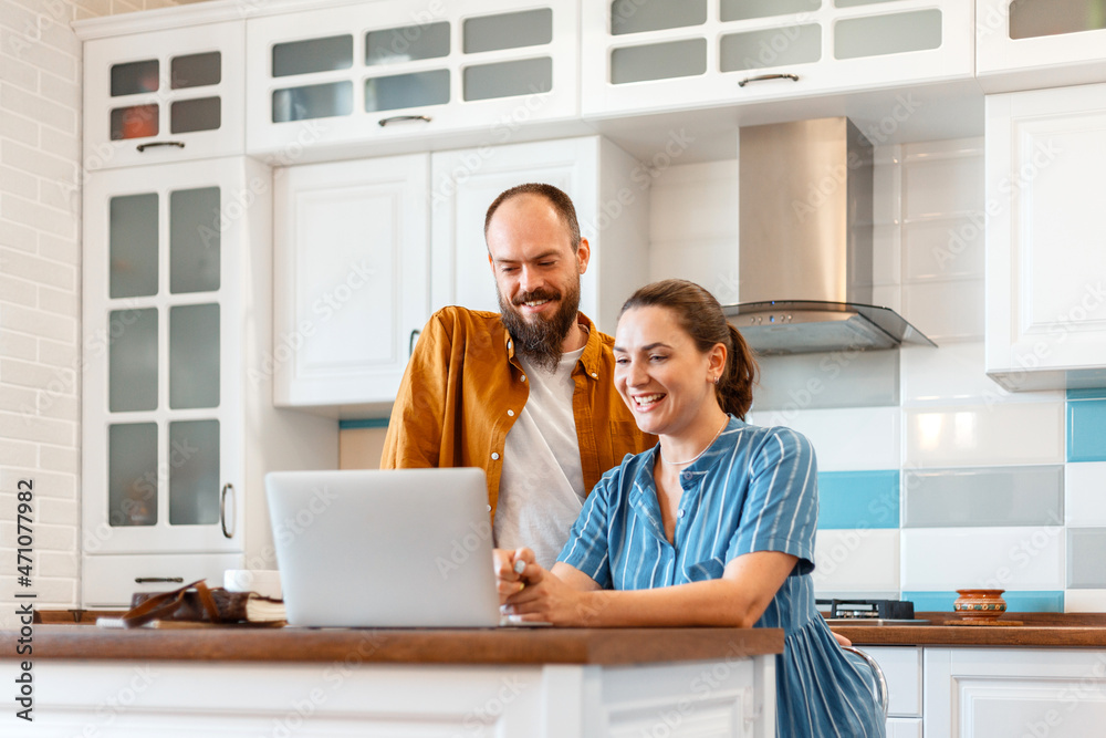 Smiling young married couple talking via video call using laptop at home in kitchen interior. Woman and man happy to hear good news from e-mail in laptop. Video calls communication. Smiling young married couple talking via video call using laptop at home in kitchen interior. Woman and man happy to hear good news from e-mail in laptop. Video calls communication.