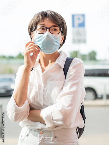 Woman puts medical protective mask on face before entering shopping mall. Coronavirus COVID-19 precautional measure. New normal.
