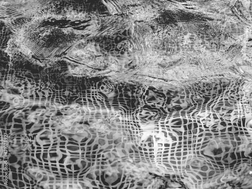 Sun beams on surface of water in swimming pool or fountain with mosaic bottom. Abstract black and white background with wavy pattern of clear transparent water.