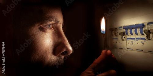 Tableau sur toile A man in complete darkness holding a burning match to investigate a home fuse box