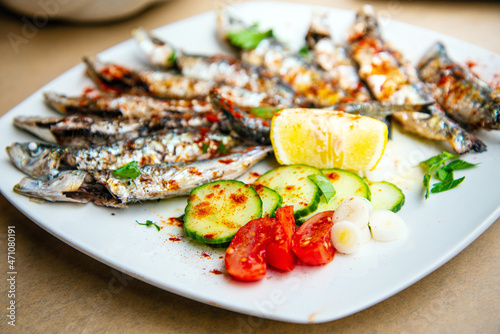 Fresh Grilled sardines served with fresh tomatoes, cucumbers slices and lemon on white plate for mediterranean healthy meal