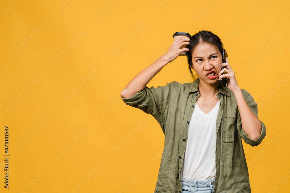 Young Asia lady talk by phone with negative expression, excited screaming, cry emotional angry in casual cloth and stand isolated on yellow background with blank copy space. Facial expression concept. Young Asia lady talk by phone with negative expression, excited screaming, cry emotional angry in casual cloth and stand isolated on yellow background with blank copy space. Facial expression concept.