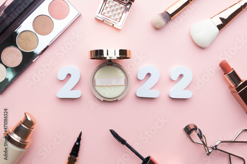 2022 Beauty cosmetic makeup products trends concept. Top view of 2022 white number with powder, lipstick, foundation, eyeshadow, brush, eyeliner and mascara on pink background. photo