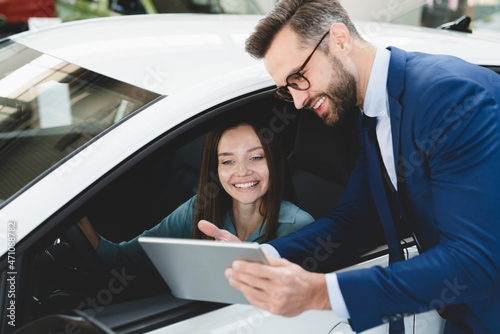 Male handsome caucasian shop assistant showing explaining to a female client customer car options information on digital tablet before buying choosing new car auto photo