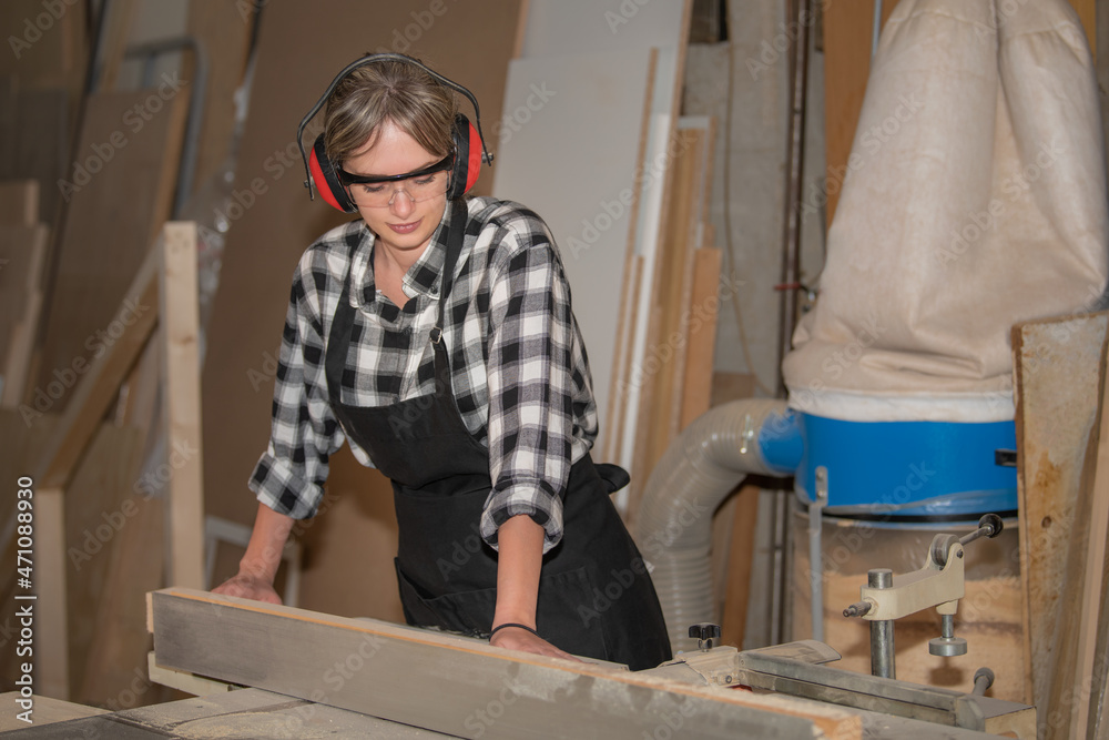 Young woman as a carpenter with safety glasses and hearing protection works on planing machine Young woman as a carpenter with safety glasses and hearing protection works on planing machine