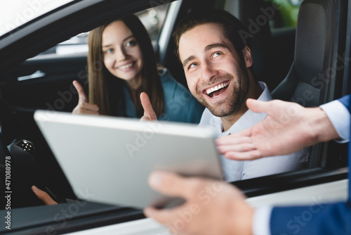 Male handsome caucasian shop assistant showing explaining to family couple clients customers car options information on digital tablet before buying choosing new car auto © InsideCreativeHouse