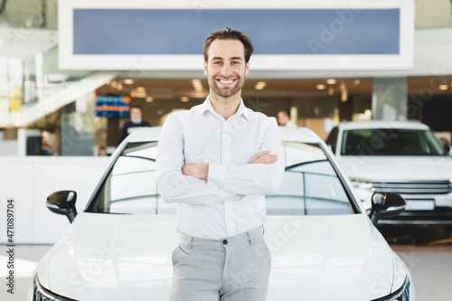 Successful rich man in formal clothes buying purchasing new expensive car automobile in auto trader shop store dealer, leaning on the car with his arms crossed © InsideCreativeHouse