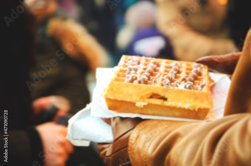 Blurred photo of man carefully carrying a Belgian waffle in Christmas market crowd. Paris, France.
