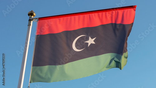 National flag of Islamic republic of Libya on a flagpole in front of blue sky with sun rays. Diplomacy concept.