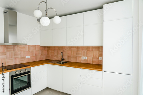 Fototapeta Naklejka Na Ścianę i Meble -  Modern kitchen interior with furniture and electrical appliances. Trendy stylish kitchen in white, beige-rose and wooden clear tones.