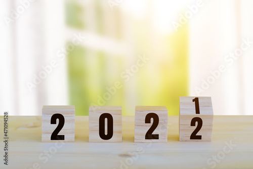 Flipping wooden cubes blocks placed on table in front of white window, curtain, tree and sunlight background for change year 2021 to 2022. New year and holiday concept.
