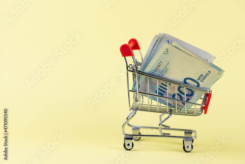 Israel money shekel banknotes in shopping cart on yellow background. Exchange Rates and buy sell currency concept. photo
