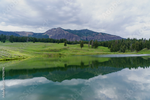 Trout Lake Trail in Yellowstone National Park on a cloudy summer day - a mountain reflects in a blue lake, with green grass on the hillside in the distance © Sitting Bear Media