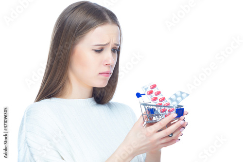 Studio shot of upset disappointed girl holding in her hands a small shopping cart full of expensive pills and medicine, isolated on white background