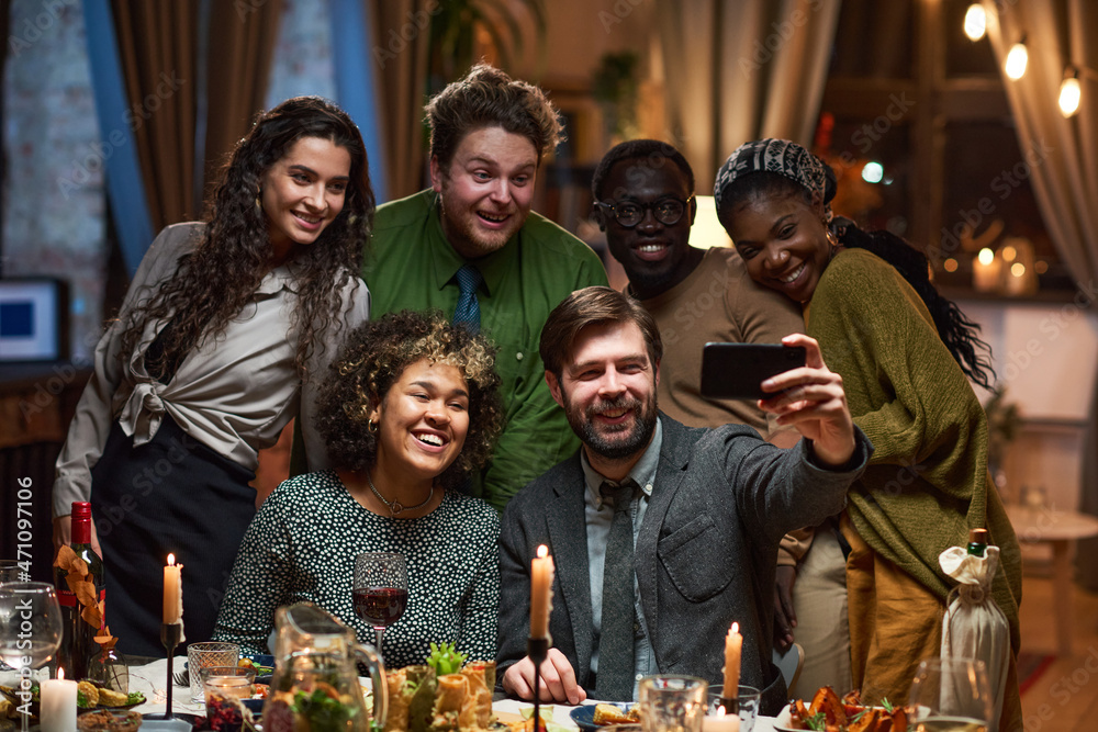 Group of happy friends smiling at camera while making selfie portrait on mobile phone at dining table Group of happy friends smiling at camera while making selfie portrait on mobile phone at dining table