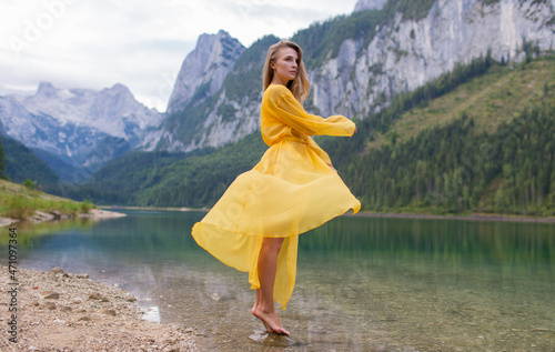 Young beautiful girl in a light yellow dress by the lake in the mountains