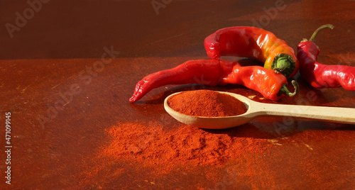 Paprika seasoning in a side view wooden spoon beside peppercorns on wooden red background.