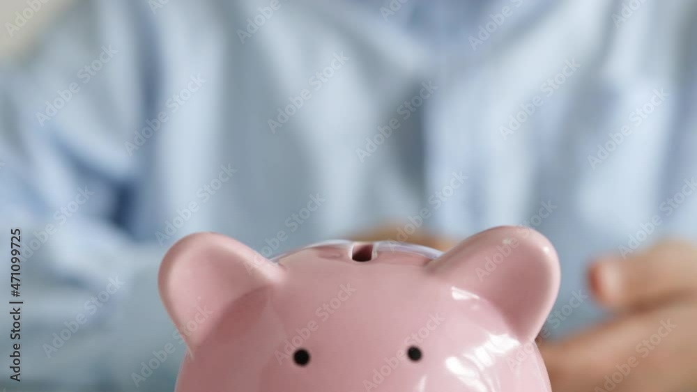 Close up of woman holding pink piggybank while woman putting coin in it. Close up of woman holding pink piggybank while woman putting coin in it.