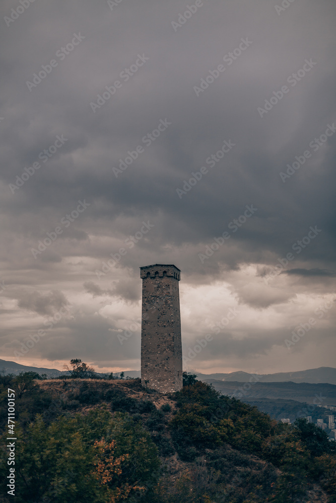 Large ancient stone tower stands on a hill in the forest. Mountain view with tragic sky. Old architecture, historical heritage, medieval tower