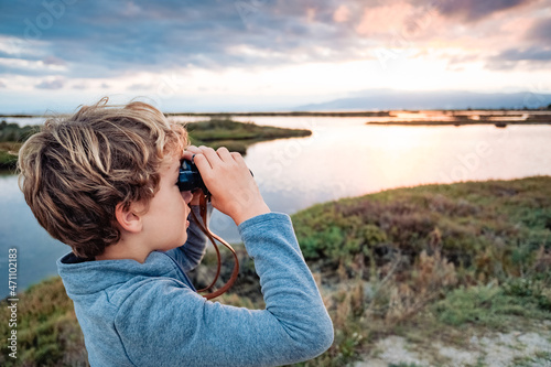 A young boy observes birds with binoculars in a nature park during his nature vacation.