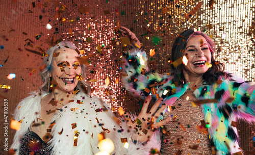 Senior females in fur coats celebrating together in studio under colorful confetti © Artem Varnitsin