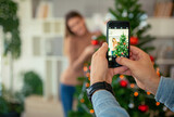 Man photographing his girlfriend while decorating Christmas tree