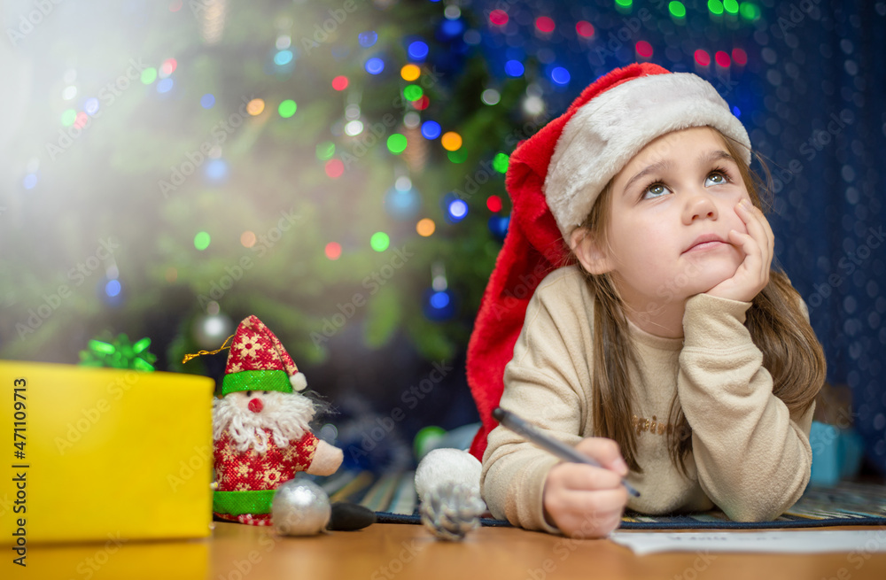 a girl lies on the floor in a New Year's cap and writes a letter to Santa Claus a girl lies on the floor in a New Year's cap and writes a letter to Santa Claus