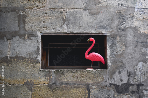 Artificial pink flamingo used as a decoration on the window. Surrounded by stone wall. Dada concept, background
