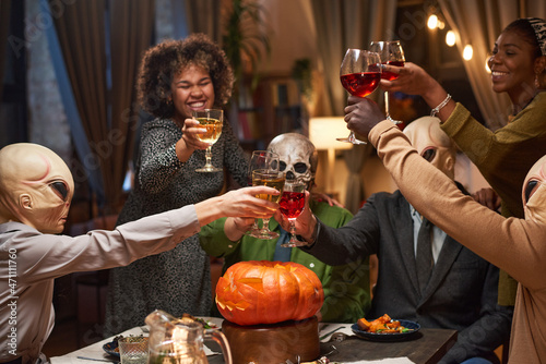 Group of of happy friends toasting with glasses of red wine and celebrating Halloween during home party