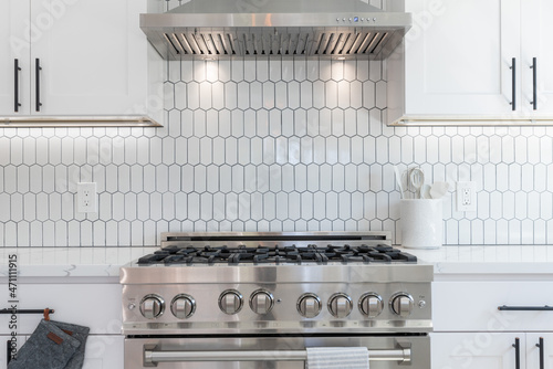 Modern kitchen details of white granite counter, gas stove, and white tile backsplash.