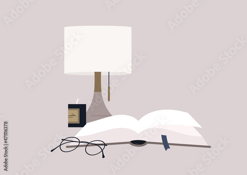 Reading scene, an open book with a ribbon bookmark in a hard cover, a scented candle, a lamp and a metal eyeglasses frame