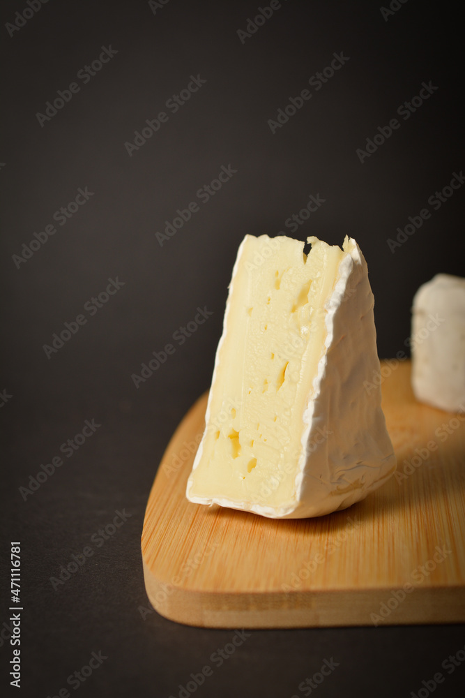 Close up of Cheeseboard with soft French Brie cheese pieces served on wooden board on dark background. Triangle piece of cheese with. Healthy Starter, appetizer, snack or dessert
