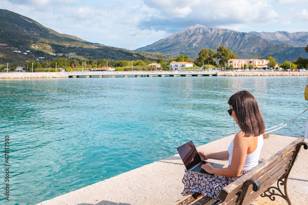Fototapeta premium smiling woman freelancer working on laptop outdoors at city harbor