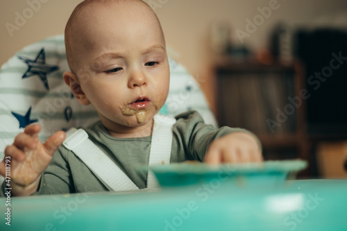 Adorable little baby eating his dinner and making a mess