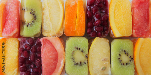 fruits frozen in ice cubes, orange, grapefruit, lemon, kiwi, pomegranate. are laid in a row on a marble table