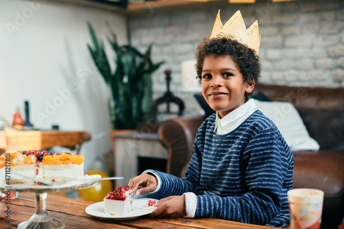 Happy African American Birthday boy eats slice of cake at home and looking at camera.