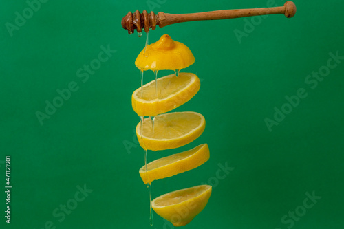 sliced lemon with honey and honey dripper, levitating on green background