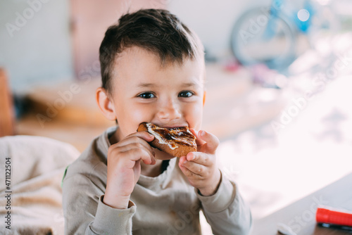 a cute boy is sitting outside eating bread with butter and jam