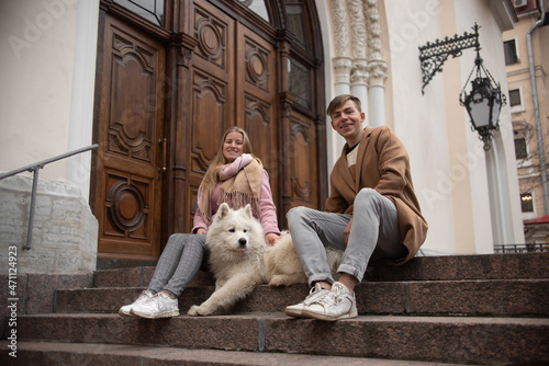 a couple in love a guy and a girl are walking in the parks of a beautiful city in autumn in November with a friend of a white fluffy big dog