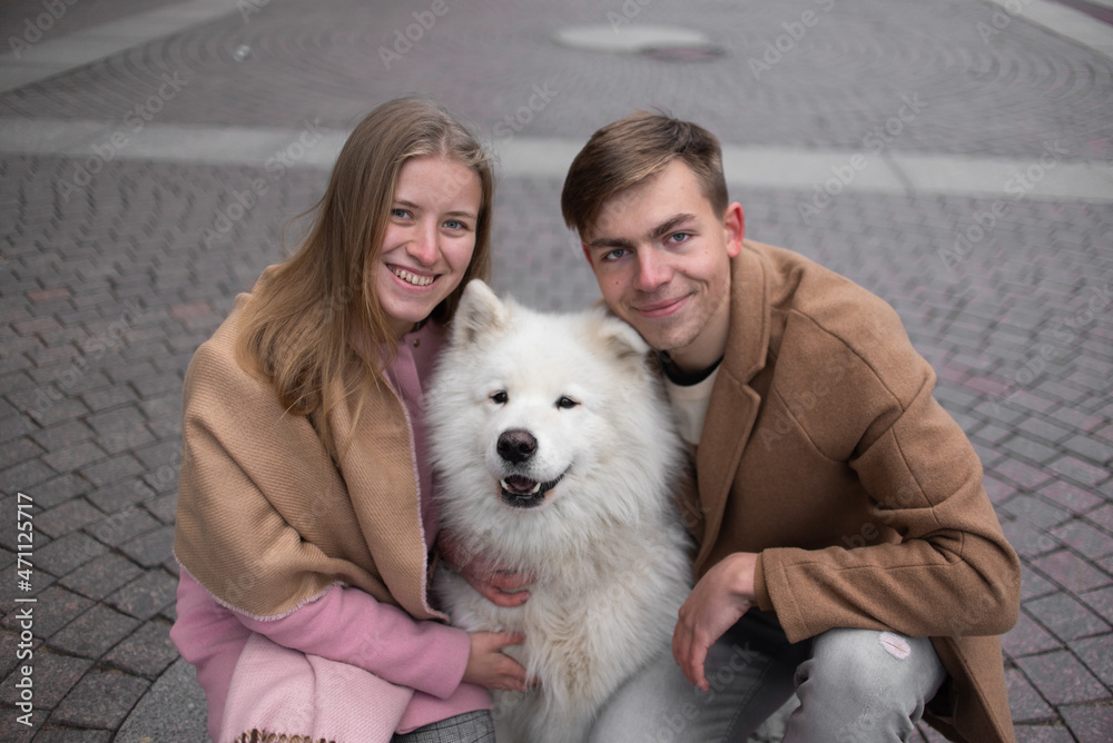 a couple in love a guy and a girl are walking in the parks of a beautiful city in autumn in November with a friend of a white fluffy big dog a couple in love a guy and a girl are walking in the parks of a beautiful city in autumn in November with a friend of a white fluffy big dog