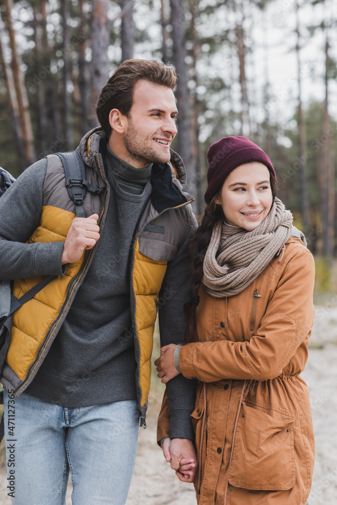 happy young couple in autumn outfit looking away while walking in forest happy young couple in autumn outfit looking away while walking in forest