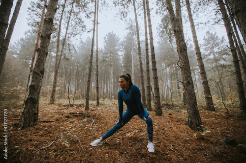 Young woman in blue track suit stretching before workout in the autumn forest